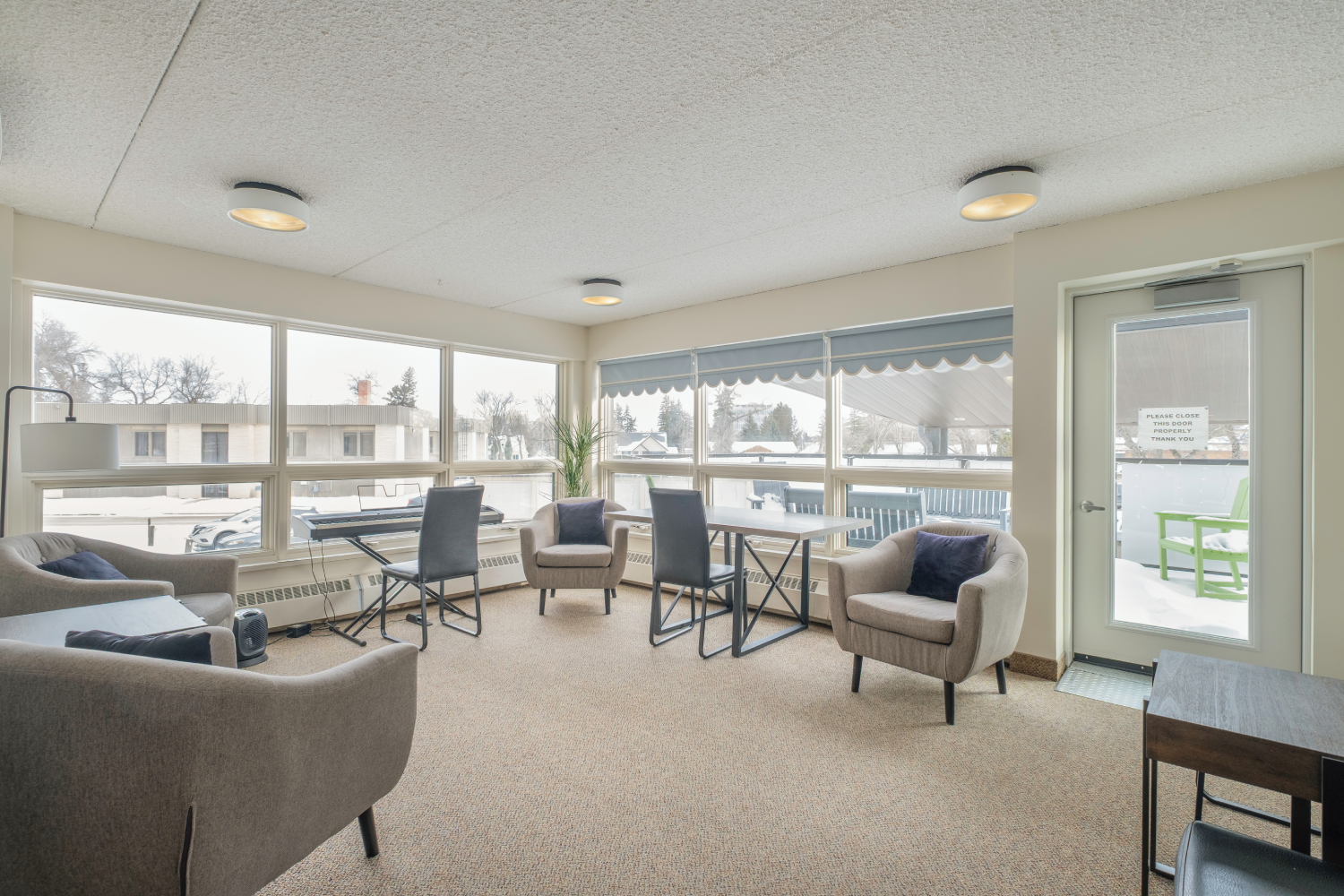 Well-lit room with large windows, comfortable seating, a small table, and a keyboard, creating a cozy space for relaxation or socializing.